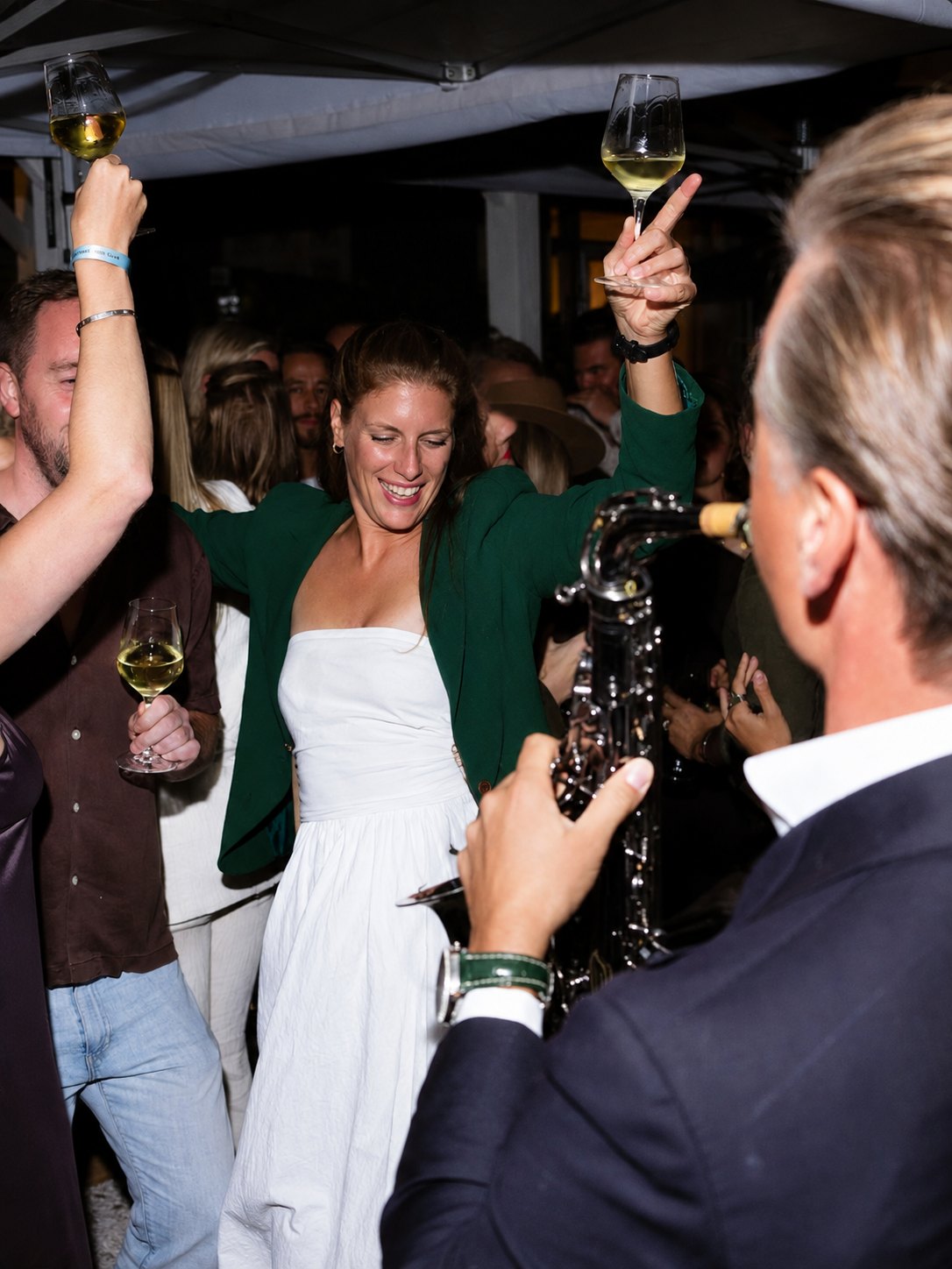 Gasten dansen met een glas wijn in de hand, een saxofonist speelt op de voorgrond