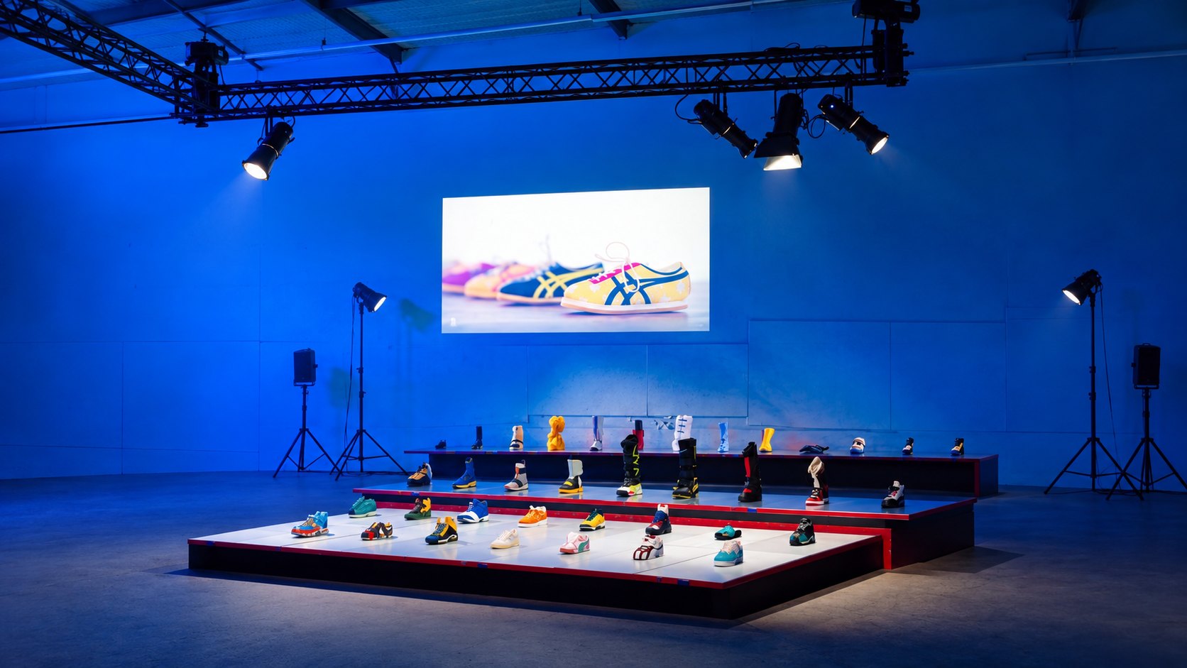 Sneakers op verlichte plateaus onder theaterspots, in een hal met blauw licht