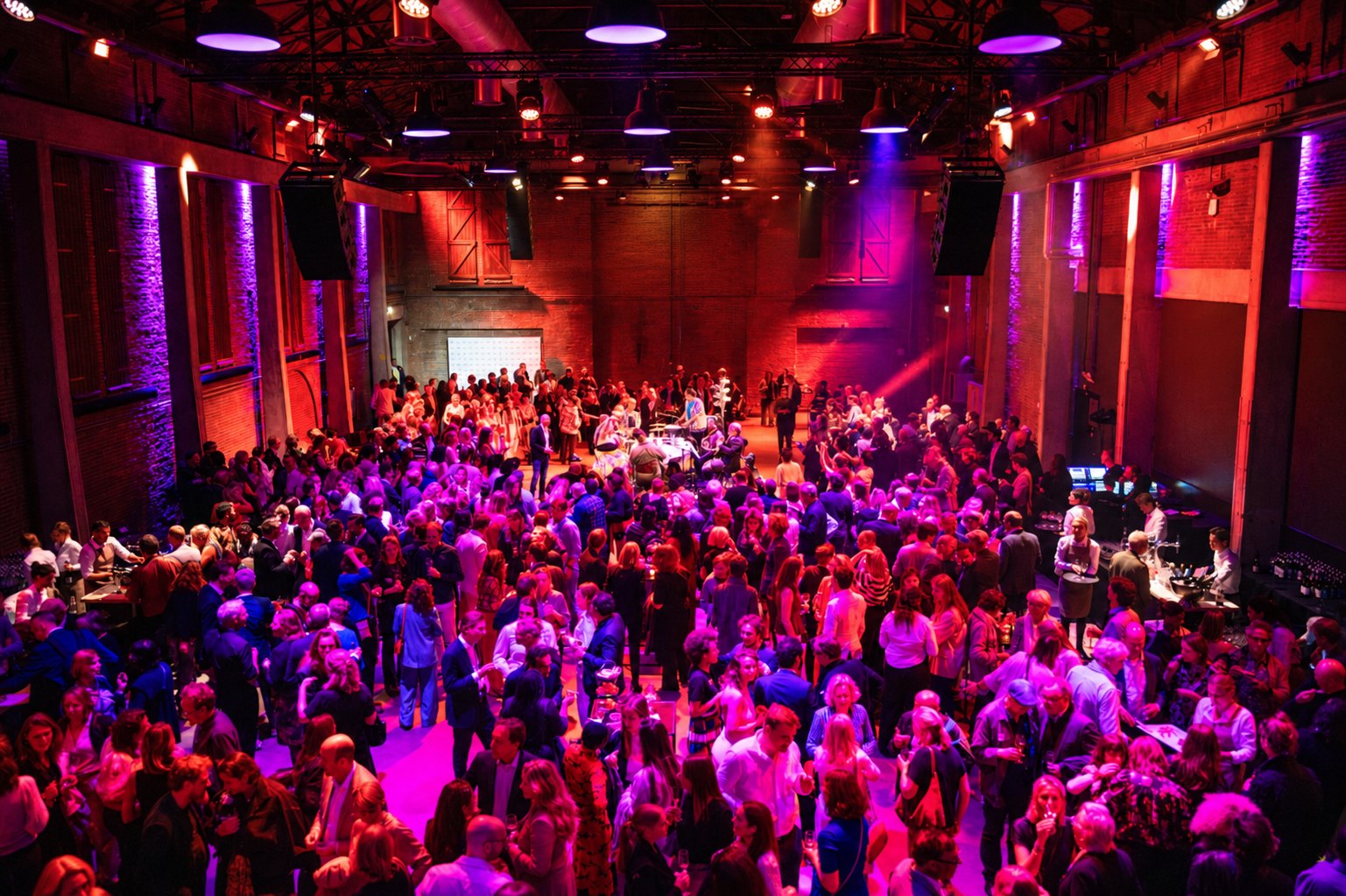 Volle industriële zaal met publiek, in rood en paars licht