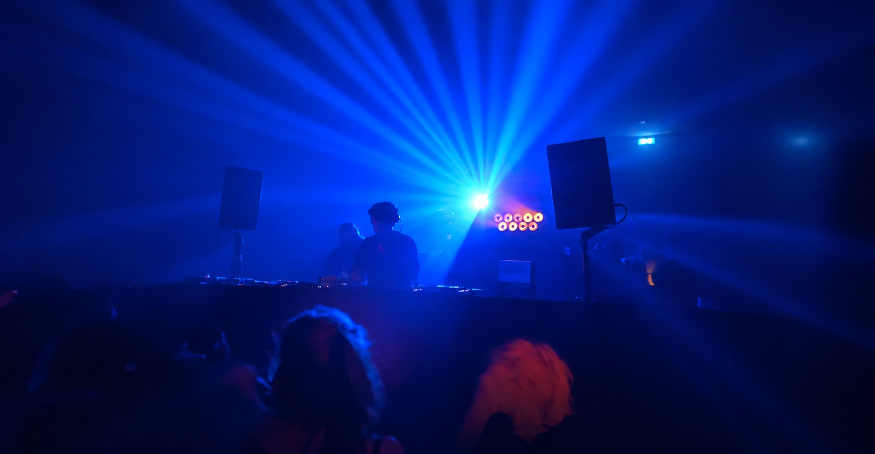 Dansvloer in blauw en rood licht, een dj achter de booth in de nevel