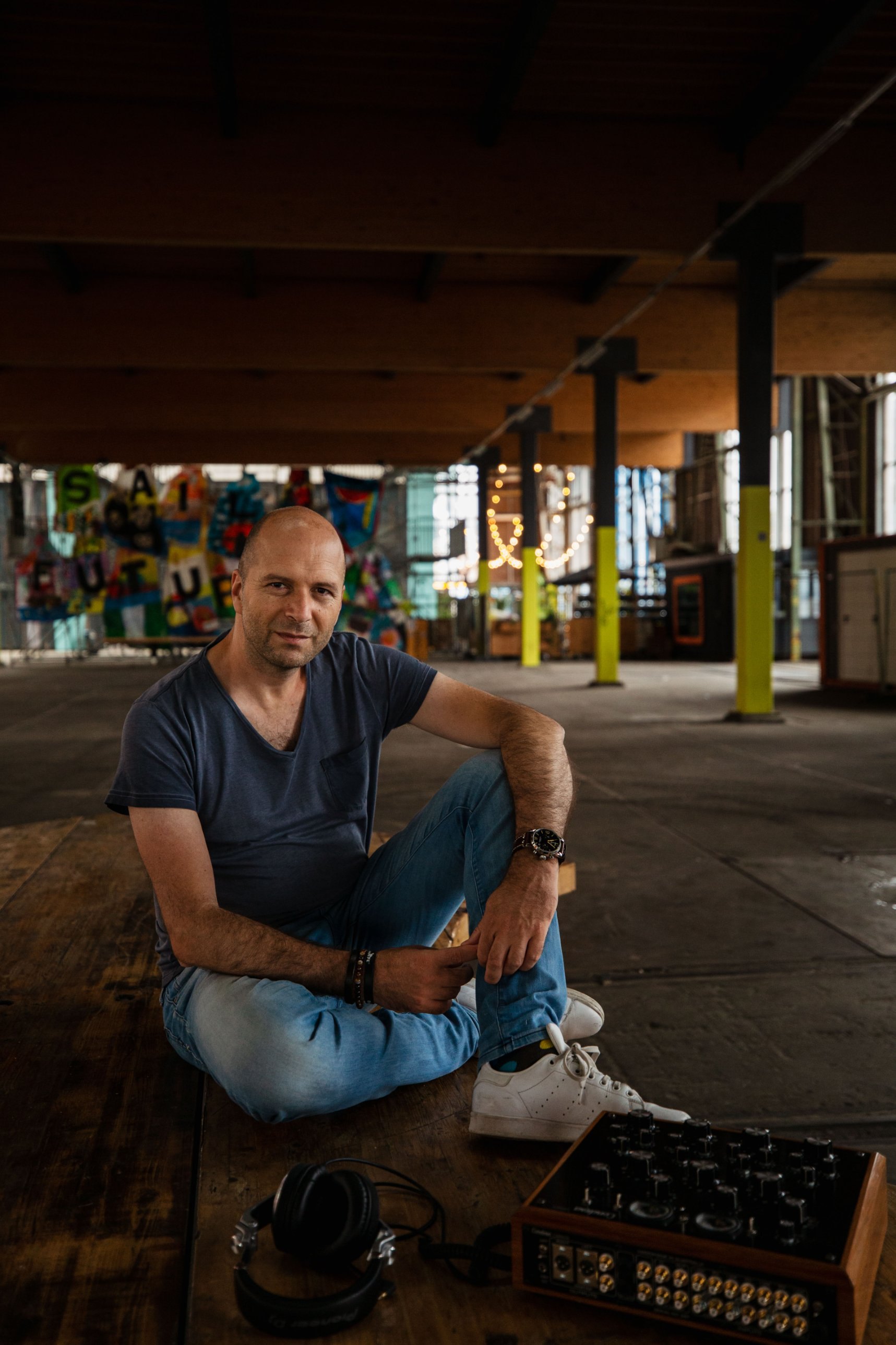 Maarten Versteeg zittend op een houten vloer in een industriële hal, met een koptelefoon en een rotary mixer voor zich